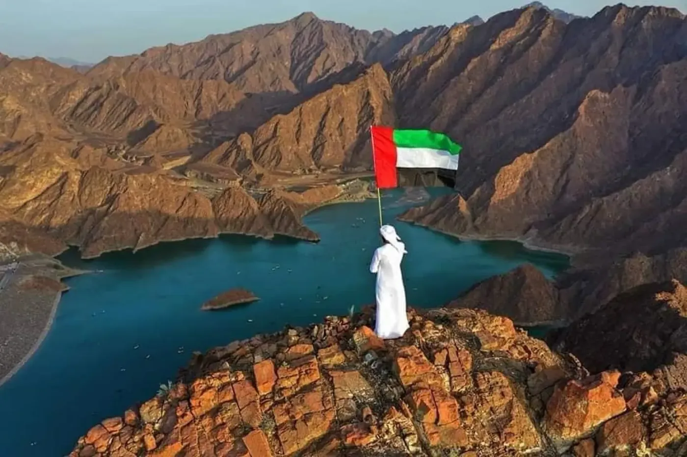 Man in white kandura holding UAE flag overlooking Hatta Dam - best viewpoint